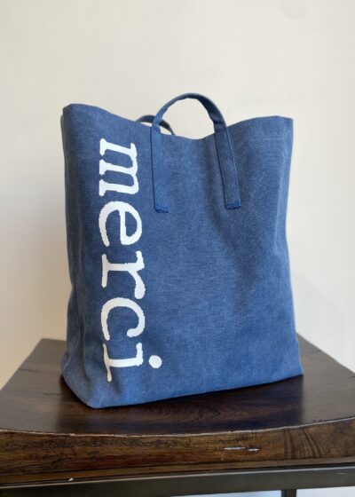 A Blue Color Tote Bag With Merci Wording